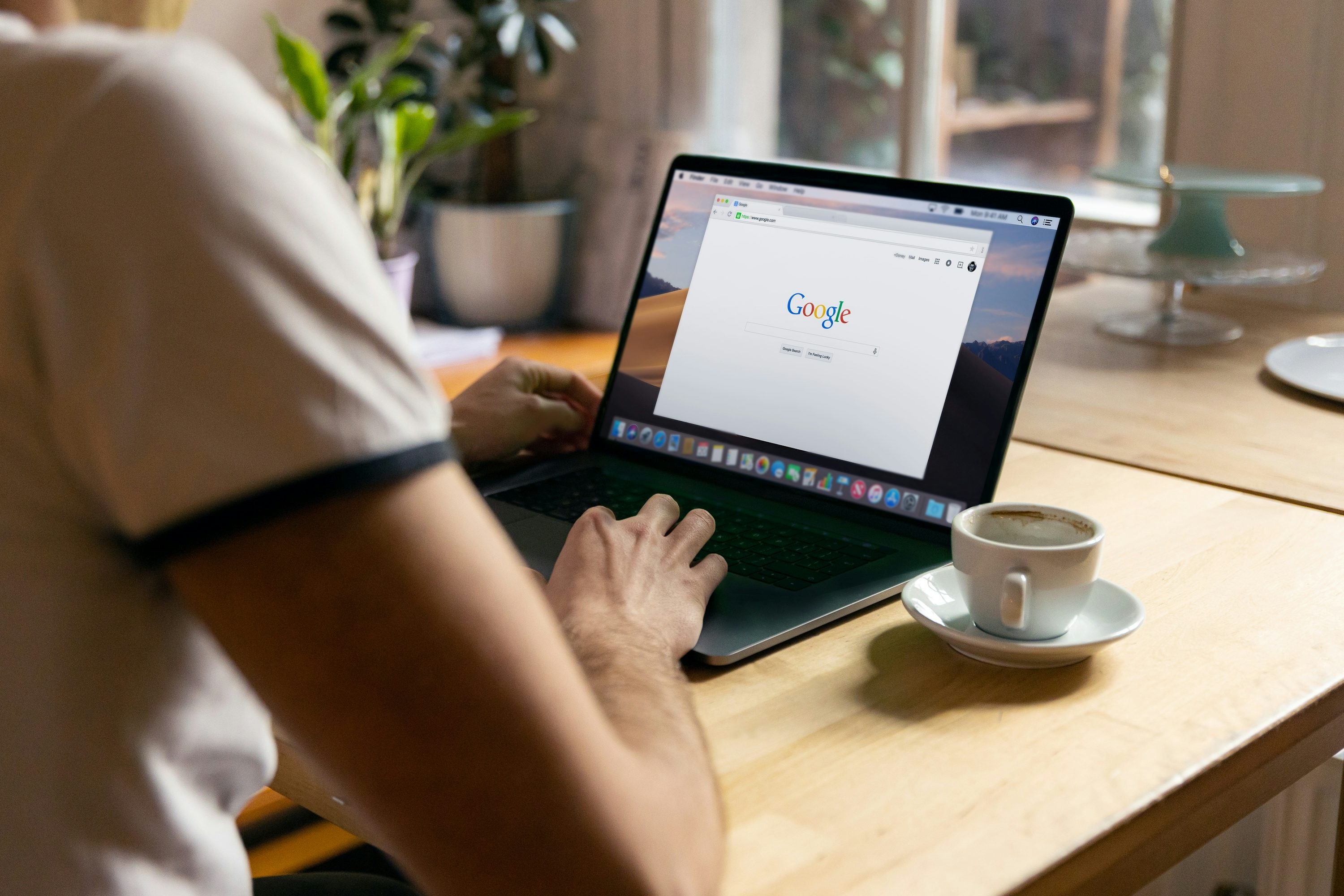Utilisateur ank sur un ordinateur portable ouvert sur une page Google, assis à une table en bois avec une tasse de café à côté.