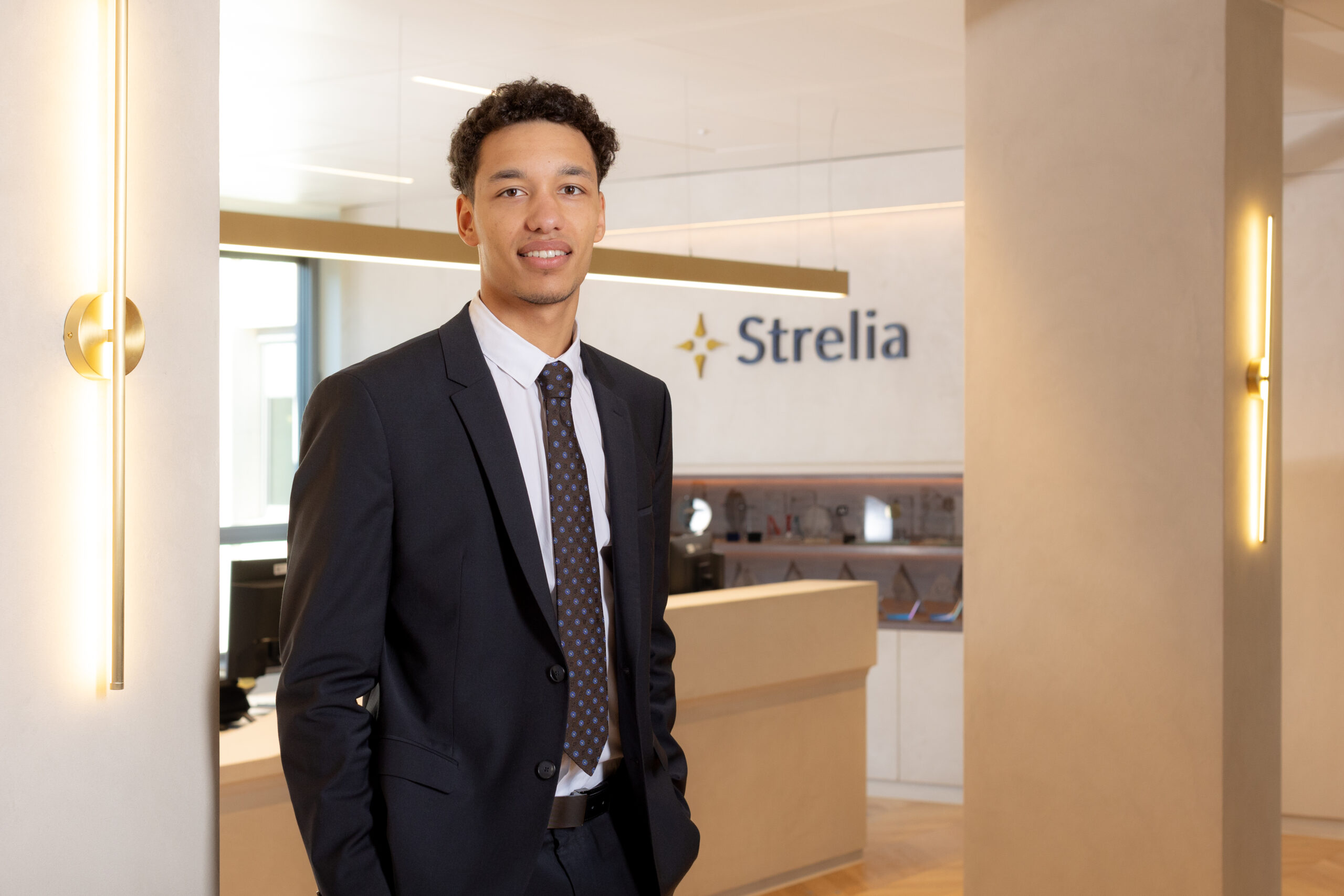Homme d’affaires en costume dans le hall d’accueil d’une entreprise, devant le logo « Strelia » et un comptoir réception.