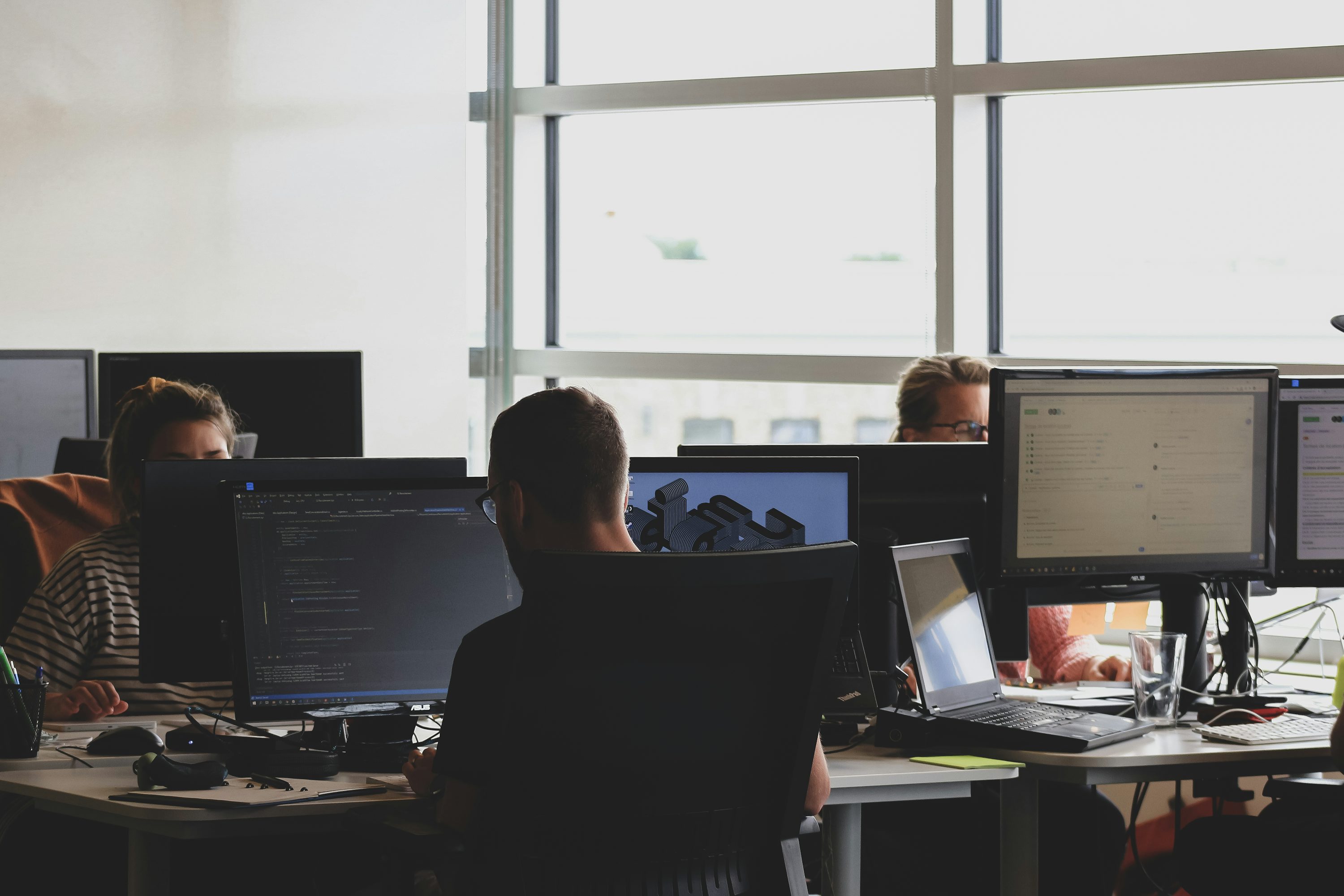 Équipe en agence digitale travaillant sur des ordinateurs et des écrans dans un espace de bureau lumineux.