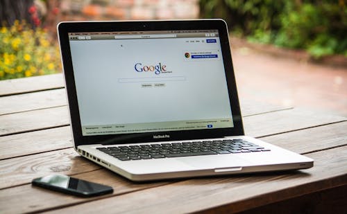Ordinateur portable affichant la page d'accueil de Google sur une table en bois, avec un smartphone à côté.