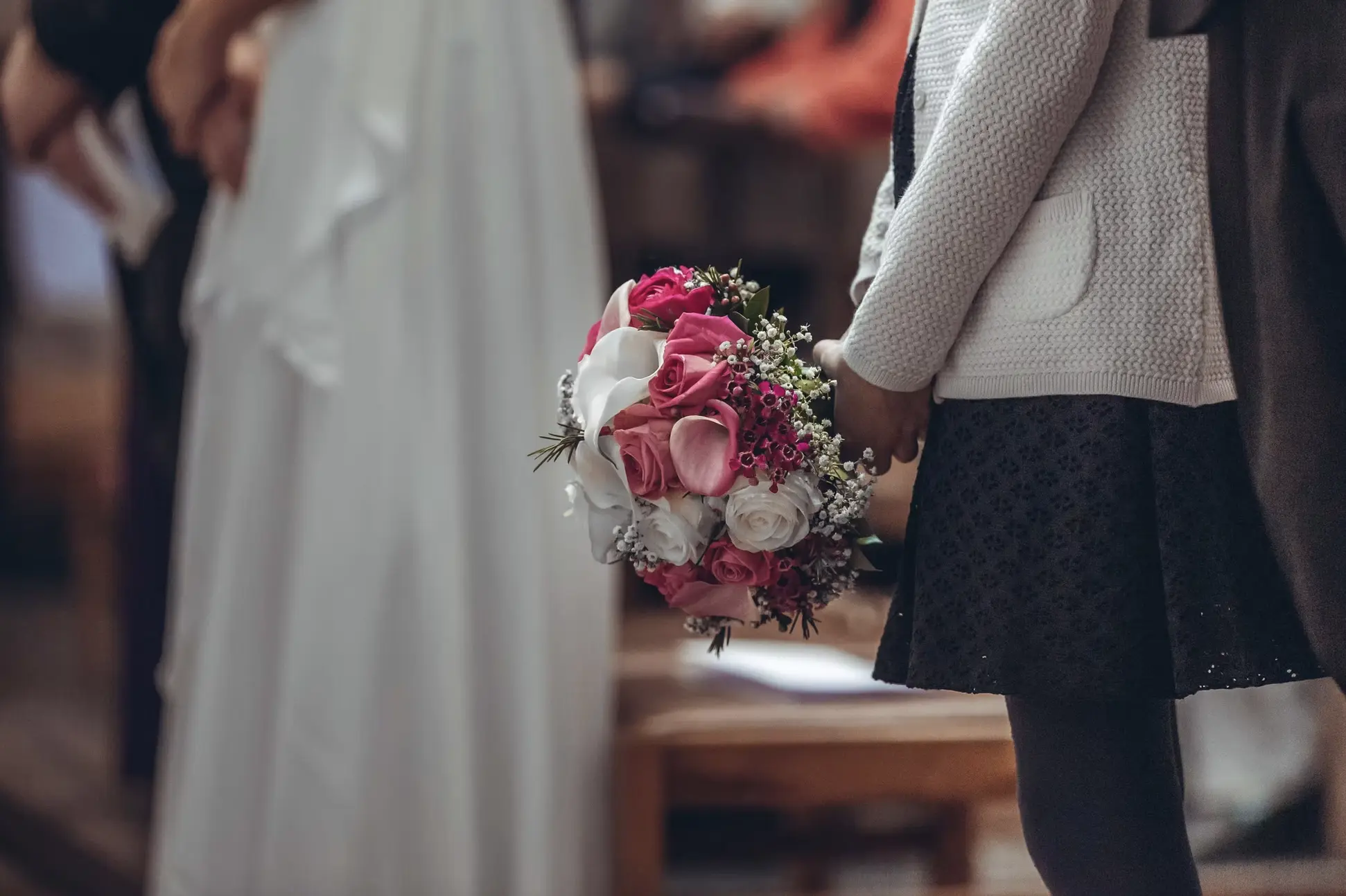 Fleur bouquet rose et blanc tenu par une enfant lors d’un événement, avec personnes floues en arrière-plan.